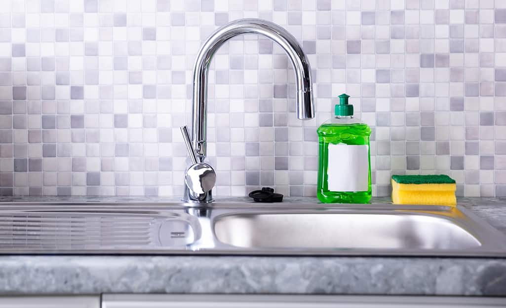 A kitchen sink with soap near the faucet A kitchen sink with soap near the faucet