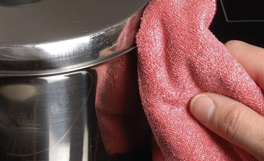 A close up of a hand wiping the outside of a deep fryer A close up of a hand wiping the outside of a deep fryer