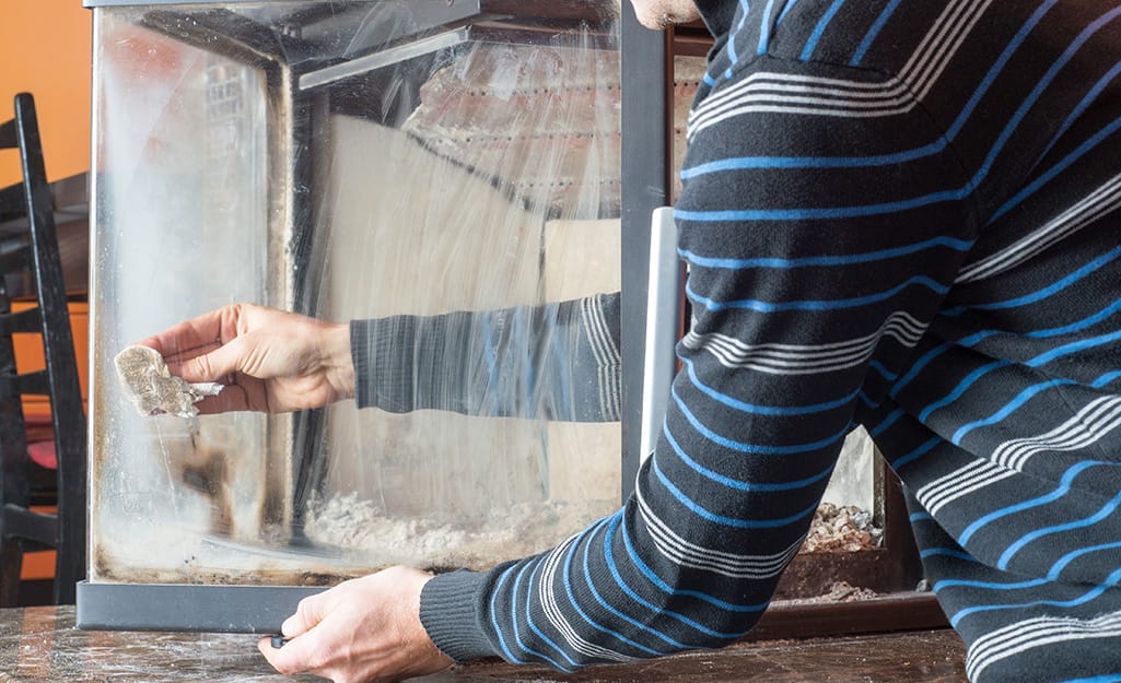 A person cleaning the inside of a glass fireplace screen. A person cleaning the inside of a glass fireplace screen.