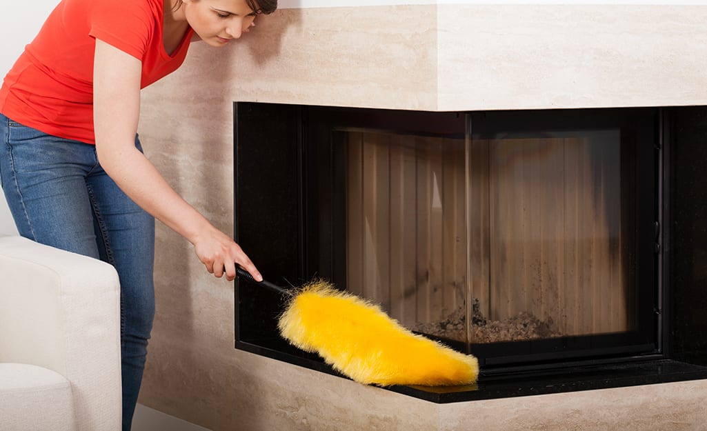 Someone dusting the outside of a fireplace. Someone dusting the outside of a fireplace.