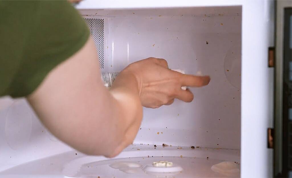 A woman sprays cleanser on the interior surfaces of a soiled microwave. A woman sprays cleanser on the interior surfaces of a soiled microwave.