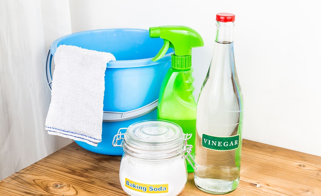 Vinegar, baking soda and a spray bottle stand next to a bucket for mixing a cleaning solution. Vinegar, baking soda and a spray bottle stand next to a bucket for mixing a cleaning solution.