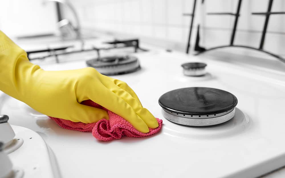 Someone wearing gloves using a cloth to wipe and clean a gas stove top. Someone wearing gloves using a cloth to wipe and clean a gas stove top.