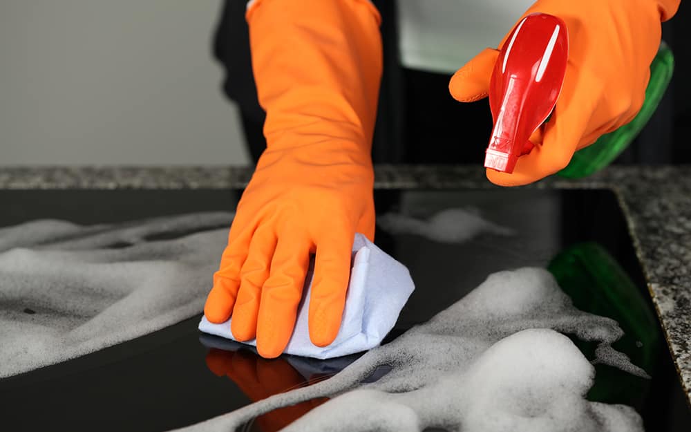 Someone wearing gloves and cleaning a ceramic stove top. Someone wearing gloves and cleaning a ceramic stove top.