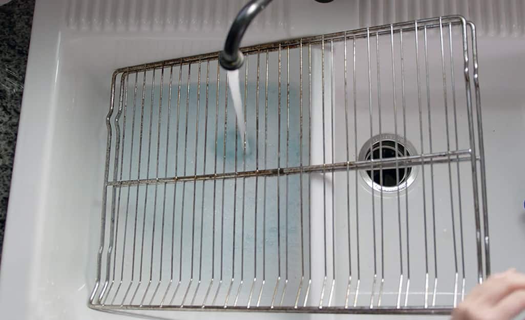 Someone cleaning oven racks in a sink. Someone cleaning oven racks in a sink.