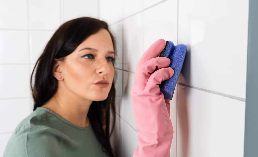 Someone using a scrubber to clean grout on a tiled wall. Someone using a scrubber to clean grout on a tiled wall.