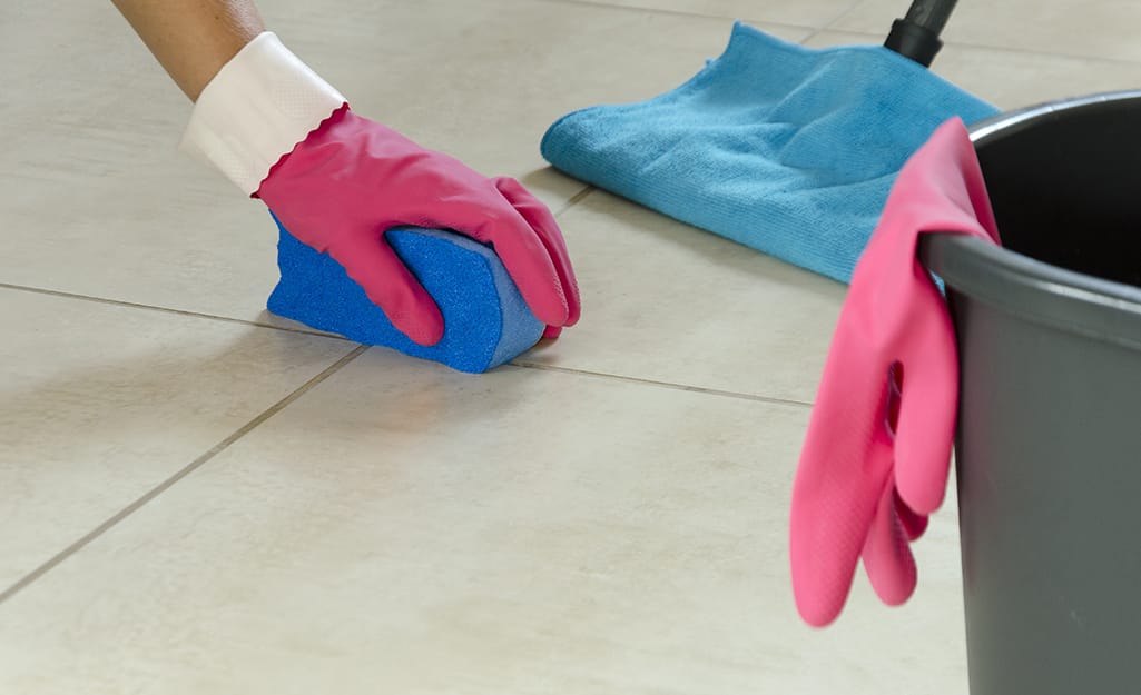 Someone cleaning grout on a tiled floor with a sponge. Someone cleaning grout on a tiled floor with a sponge.