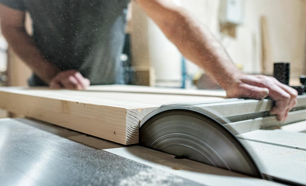 A worker trims wood board with a table saw. A worker trims wood board with a table saw.