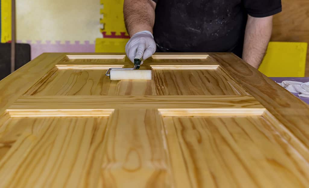 A person applies a coat of stain to the door. A person applies a coat of stain to the door.