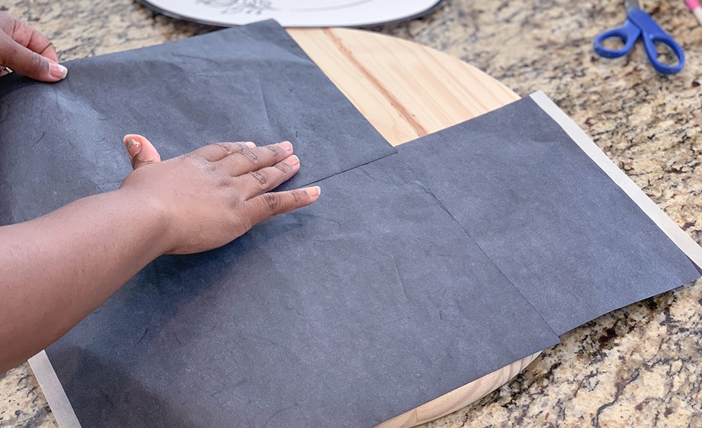 A woman lays carbon paper on top of a wood round. A woman lays carbon paper on top of a wood round.