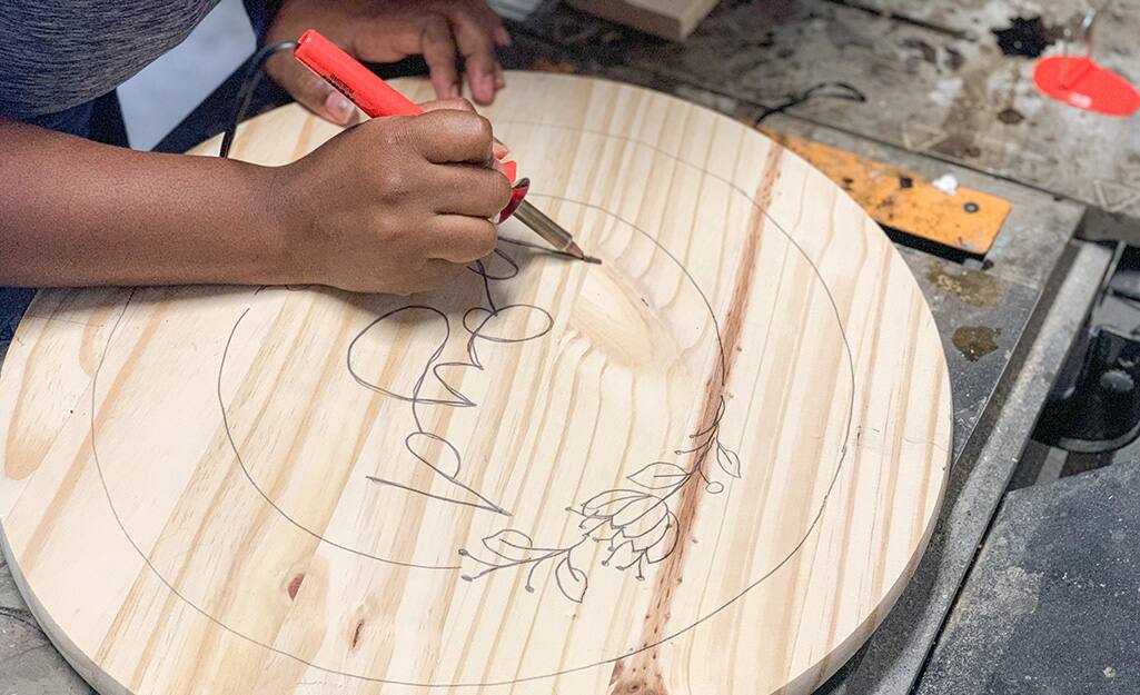 A soldering iron is used to burn the design into the wood round. A soldering iron is used to burn the design into the wood round.