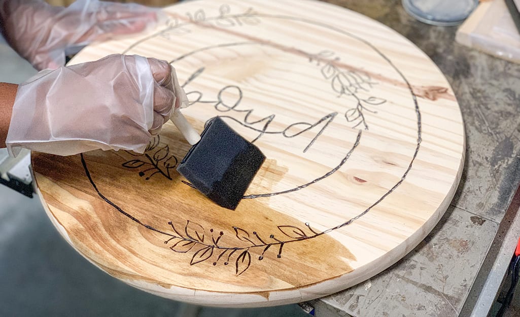 A person uses a sponge brush to stain wood. A person uses a sponge brush to stain wood.