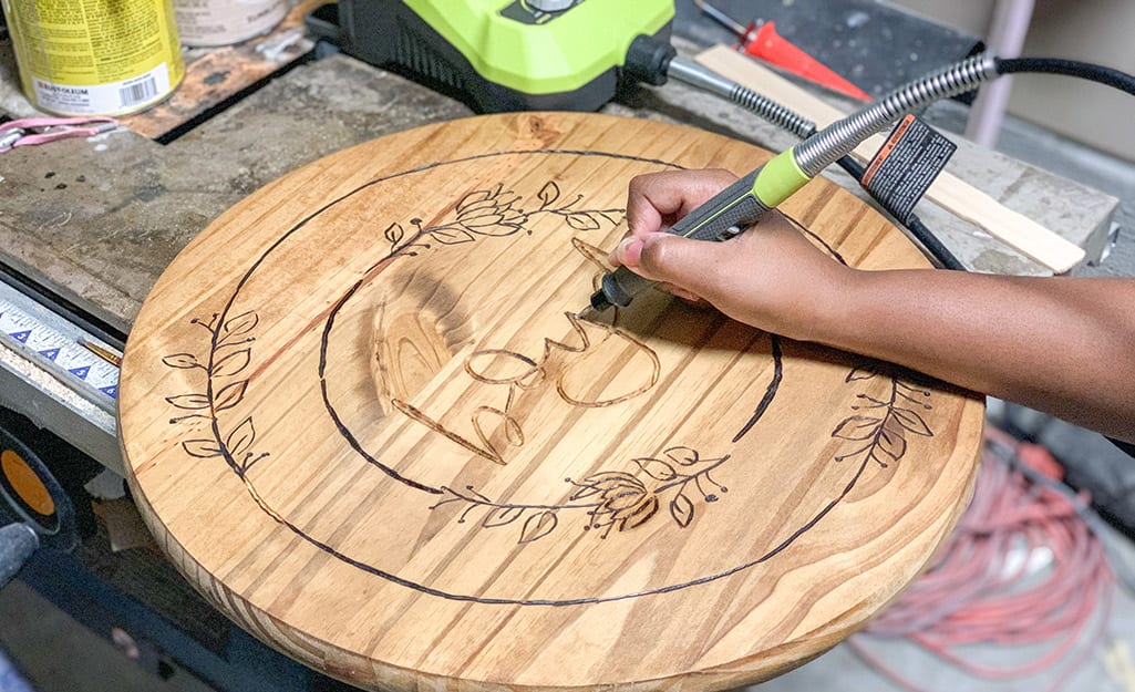 A person uses their rotary tool to carve image into wood. A person uses their rotary tool to carve image into wood.