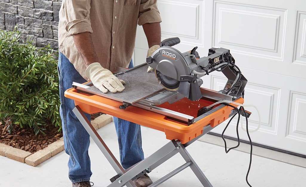 A person cuts tile with a wet saw. A person cuts tile with a wet saw.