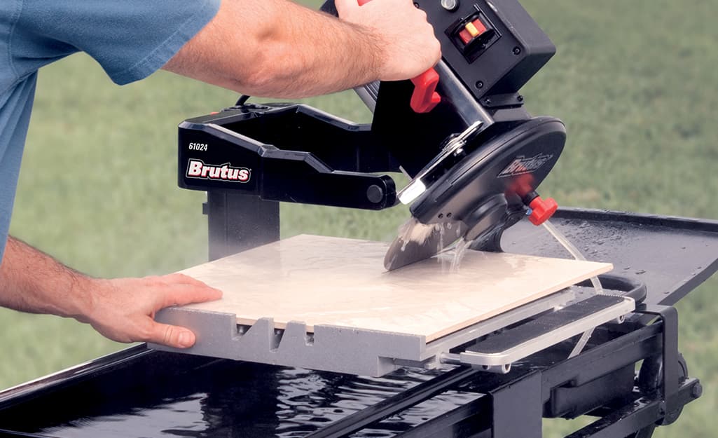 A person makes a bevel cut on a piece of tile with a wet saw. A person makes a bevel cut on a piece of tile with a wet saw.