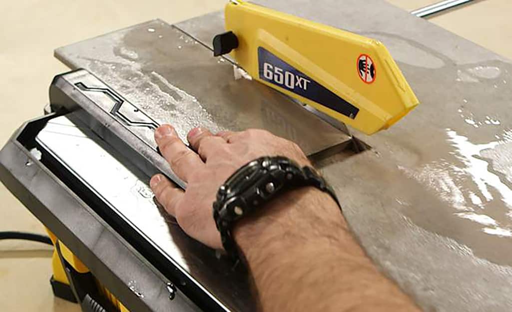 A person makes an L-shaped cut on a piece of time with a wet saw. A person makes an L-shaped cut on a piece of time with a wet saw.