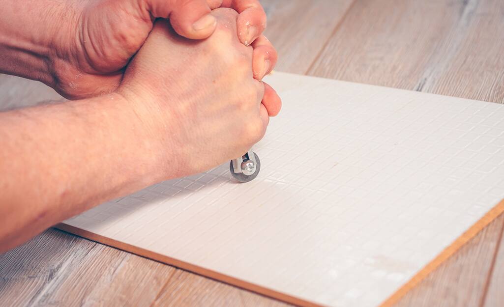A person uses a glass cutter to cut a piece of tile. A person uses a glass cutter to cut a piece of tile.