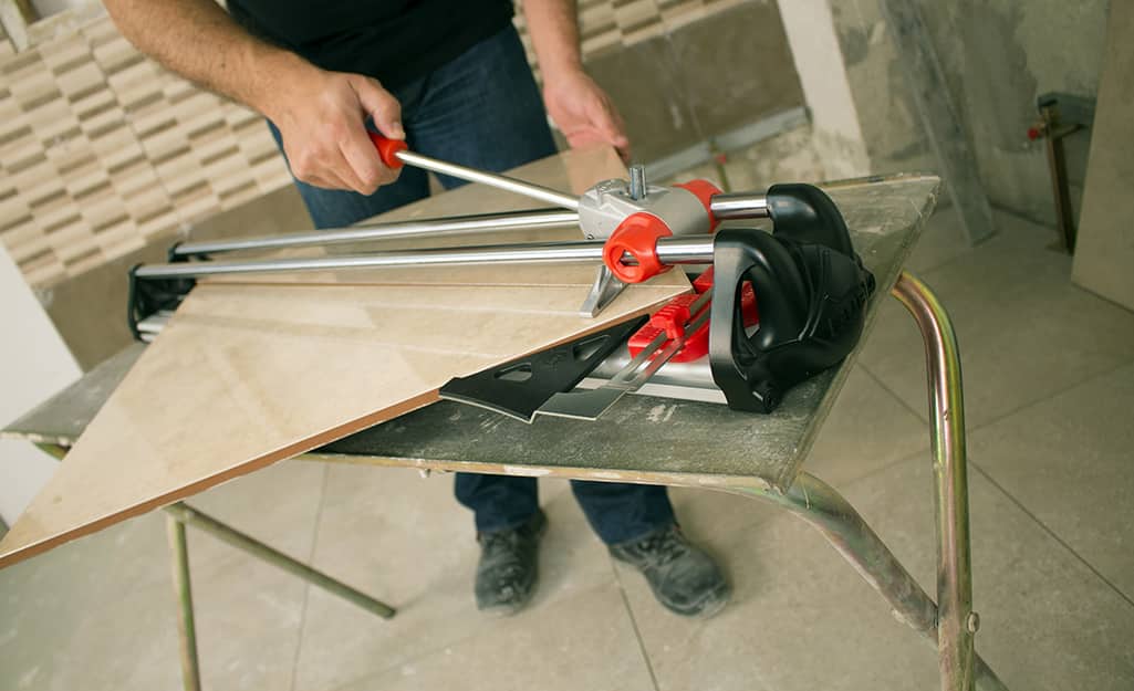 A person uses a manual tile cutter to cut a piece of tile. A person uses a manual tile cutter to cut a piece of tile.
