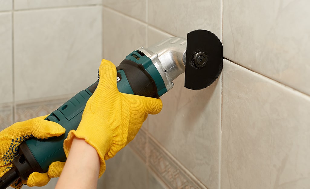 A person uses an angle grinder to cut a piece of style that's still on a bathroom wall. A person uses an angle grinder to cut a piece of style that's still on a bathroom wall.