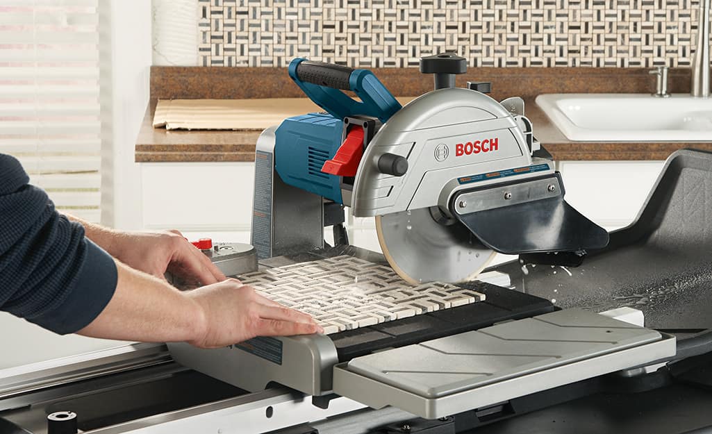 A person cuts a piece of tile with a wet saw. A person cuts a piece of tile with a wet saw.