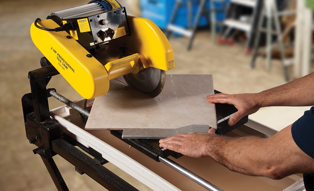 A person makes a diagonal cut on a piece of tile with a wet saw. A person makes a diagonal cut on a piece of tile with a wet saw.