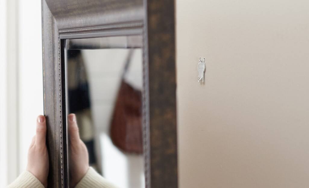 Someone hanging a mirror on a wall with a hook.