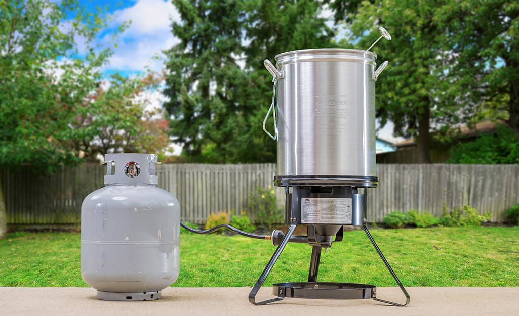 A turkey fryer and propane tank stand on a patio. A turkey fryer and propane tank stand on a patio.