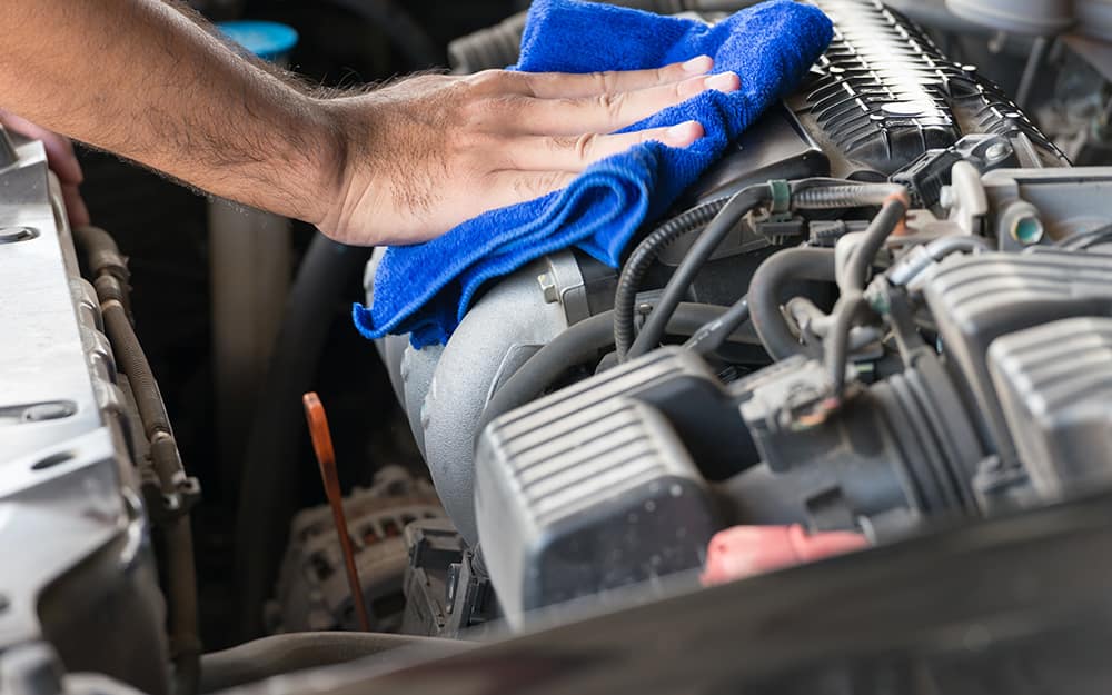 A person cleans a car's engine bay with a cloth. A person cleans a car's engine bay with a cloth.
