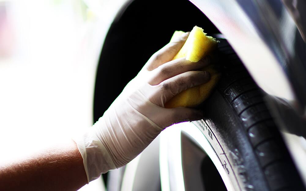 A person cleans a car tire with a sponge. A person cleans a car tire with a sponge.