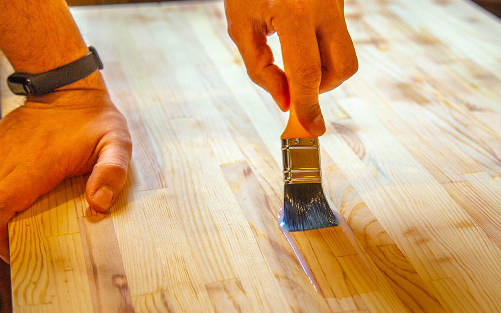 A person applying a clear finish to a wood tabletop. A person applying a clear finish to a wood tabletop.
