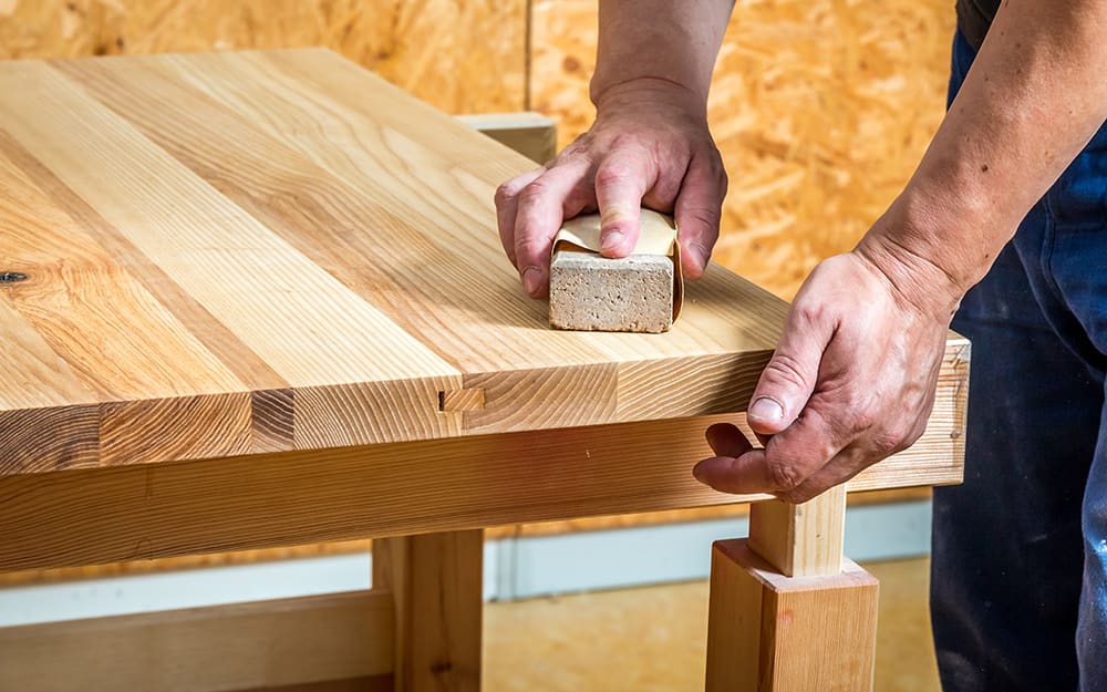 A person sanding a wood tabletop. A person sanding a wood tabletop.
