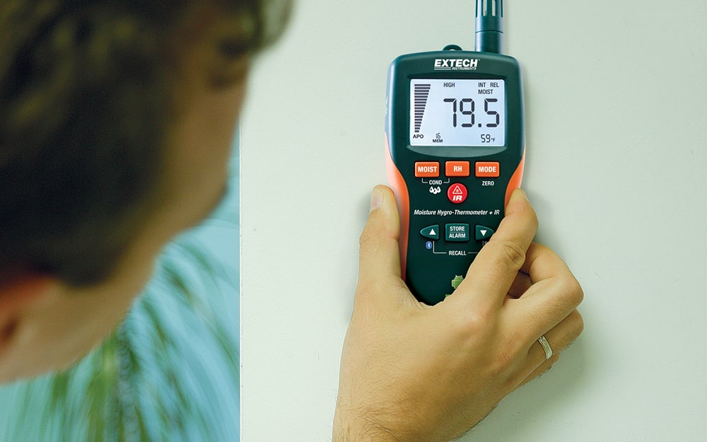 A person holding a moisture meter against a wall A person holding a moisture meter against a wall