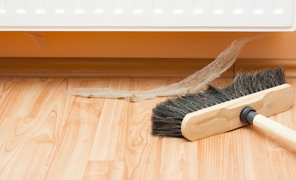 A person uses a push broom to sweep up a cobweb. A person uses a push broom to sweep up a cobweb.