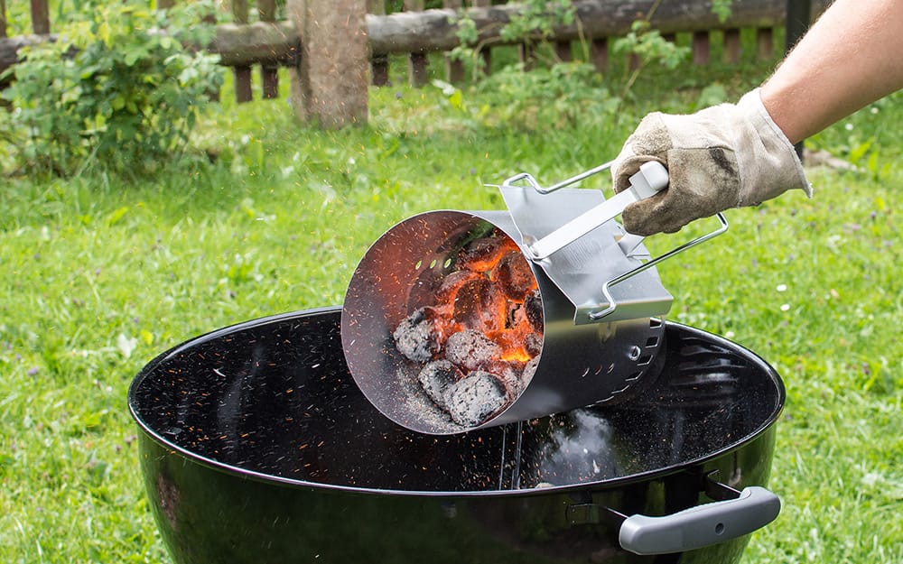 A person pouring hot charcoal into a grill. A person pouring hot charcoal into a grill.