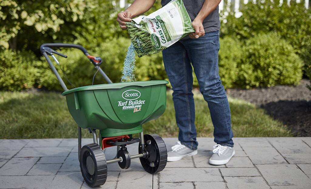 A person pouring grass seed into a lawn spreader. A person pouring grass seed into a lawn spreader.