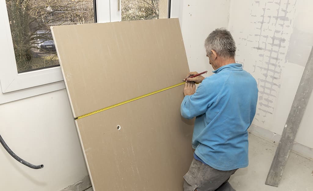 Person measuring and marking drywall. Person measuring and marking drywall.