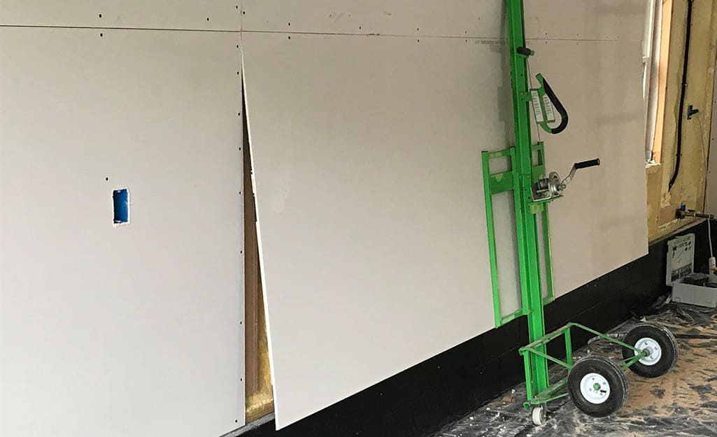 More drywall being placed on a wall using a drywall lift. More drywall being placed on a wall using a drywall lift.