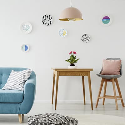 Decorative plates hung on a wall with a couch, table and chair nearby.