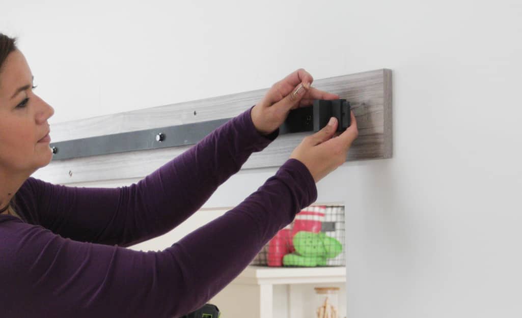 A woman installing a barn door metal track to a backer board on the wall. A woman installing a barn door metal track to a backer board on the wall.