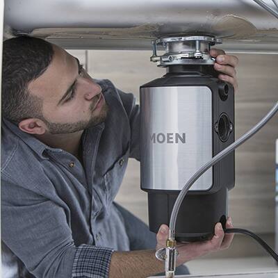 A person installs a garbage disposal under a sink.