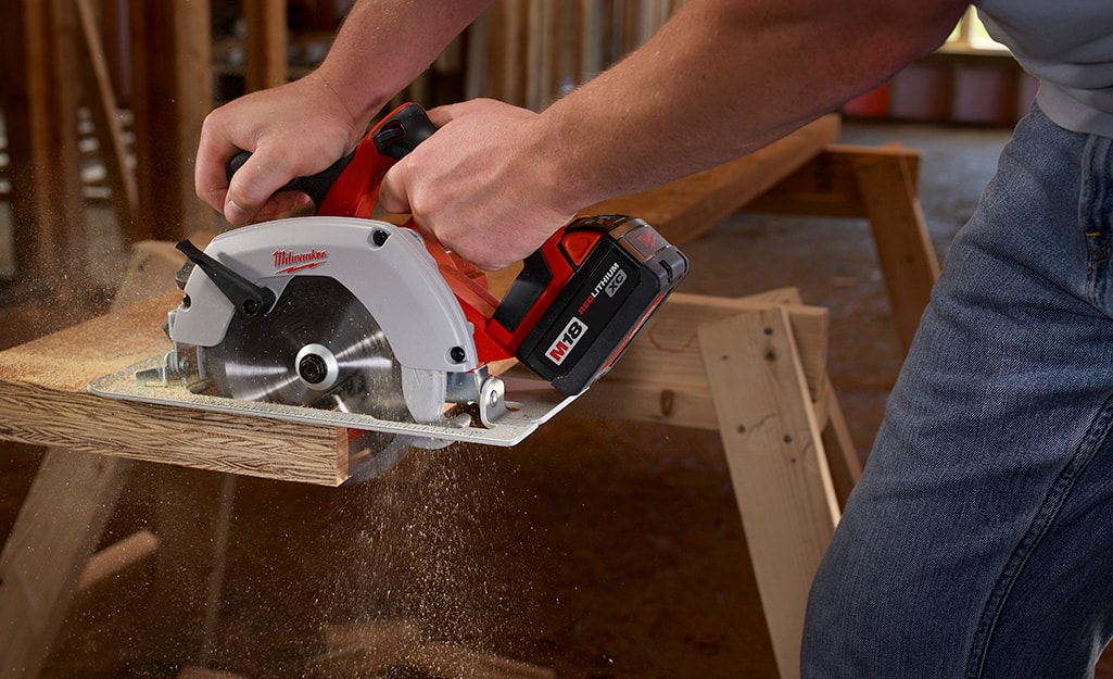 A person uses a circular saw to cut a board. A person uses a circular saw to cut a board.