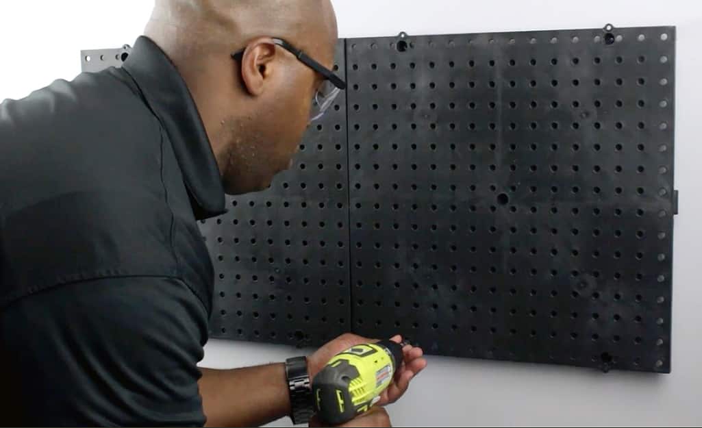 A person uses a power drill to drill holes for hanging a pegboard. A person uses a power drill to drill holes for hanging a pegboard.