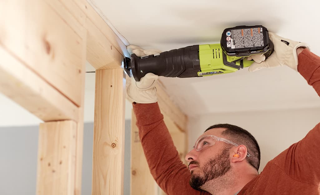 A man uses a saw to cut studs in a wall. A man uses a saw to cut studs in a wall.