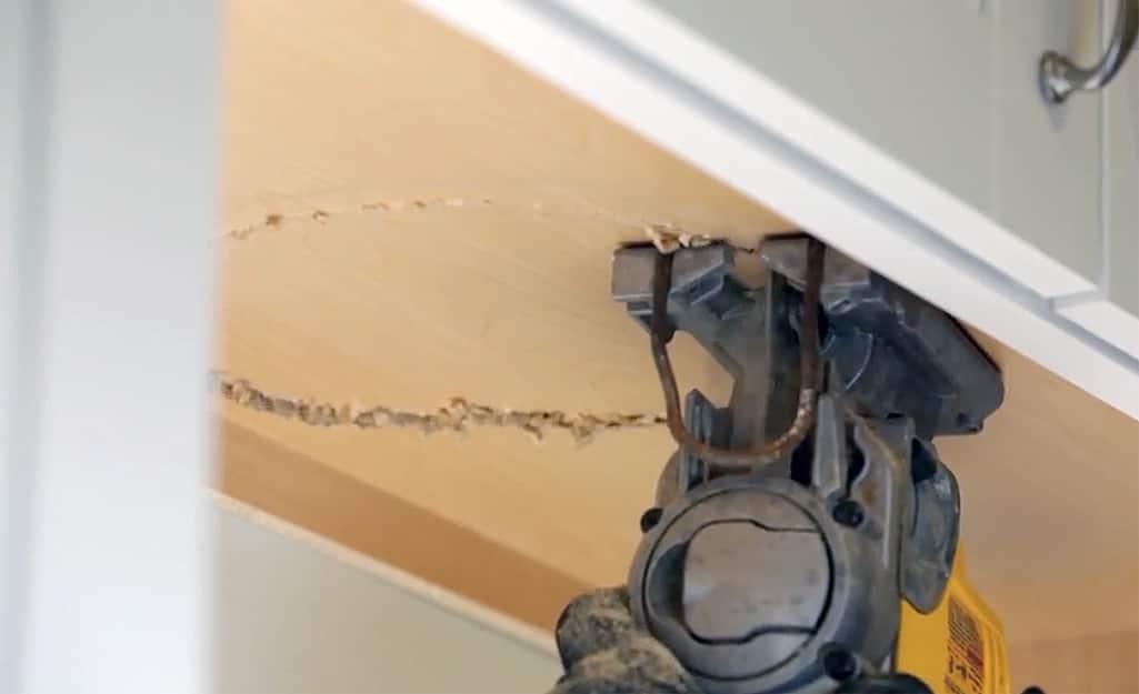 A person cuts a hole for a range hood over a stovetop. A person cuts a hole for a range hood over a stovetop.