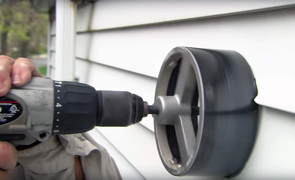 A person cuts a vent hole in exterior siding. A person cuts a vent hole in exterior siding.