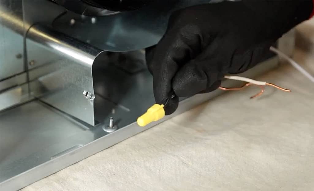 A person wires a vent hood. A person wires a vent hood.