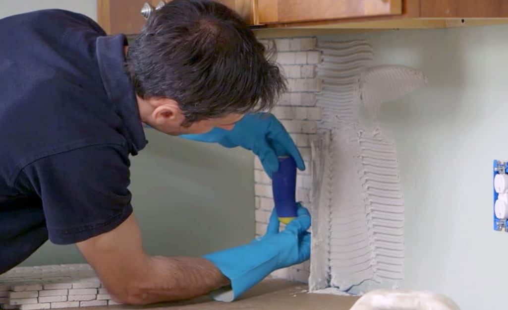A man laying tile onto a kitchen wall. A man laying tile onto a kitchen wall.