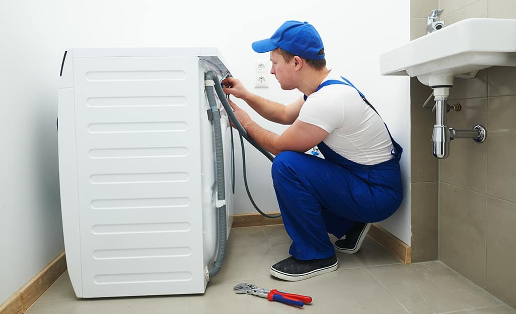 A person working on the back of a washing machine near a sink. A person working on the back of a washing machine near a sink.