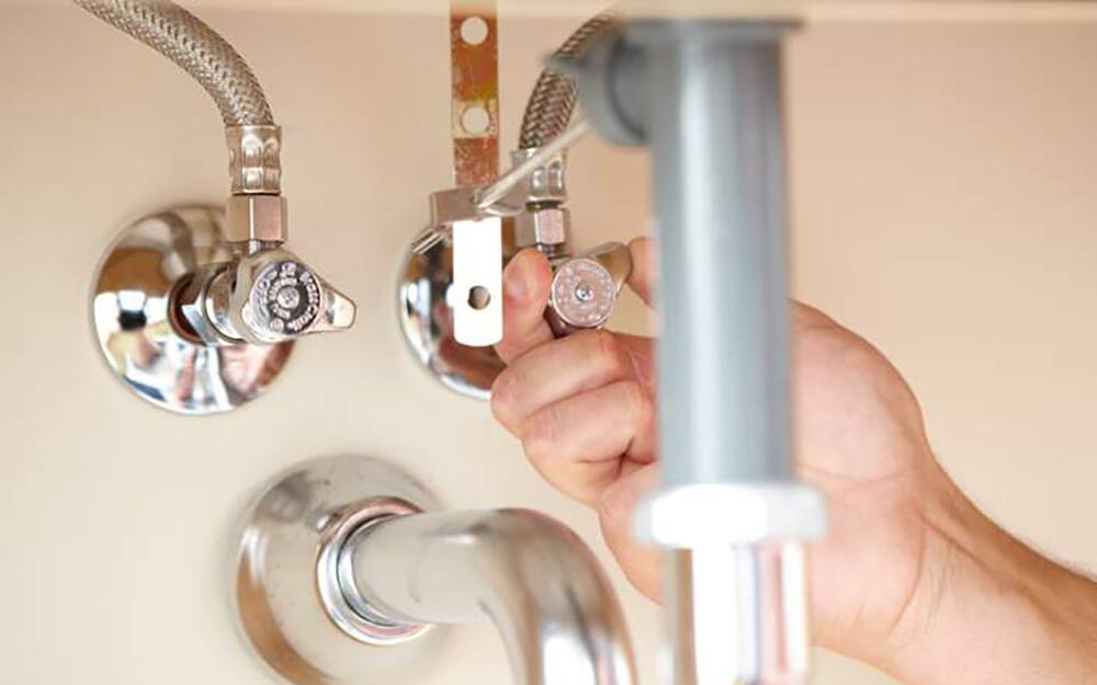 Person turning off water supply under sink. Person turning off water supply under sink.