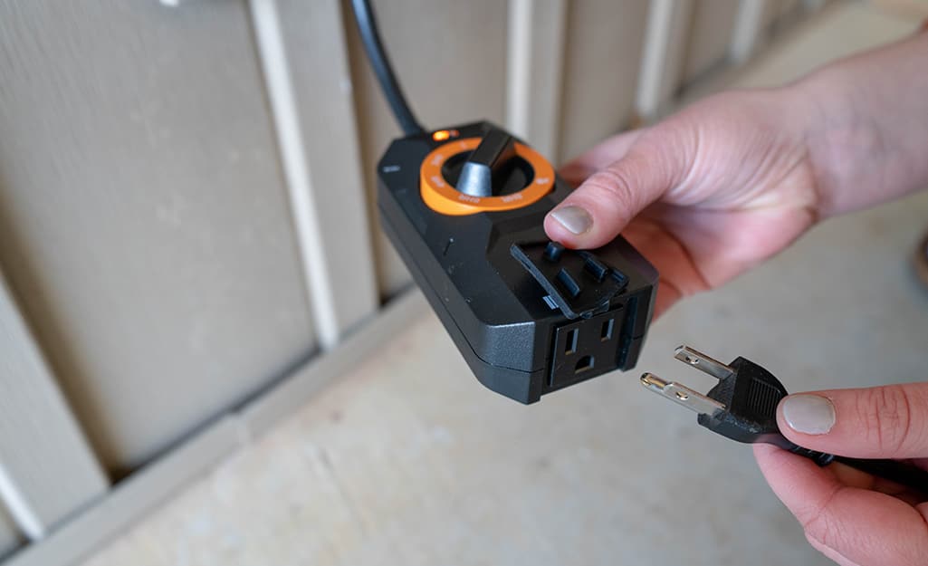 A person plugging in low voltage landscape lights to a transformer with a timer. A person plugging in low voltage landscape lights to a transformer with a timer.
